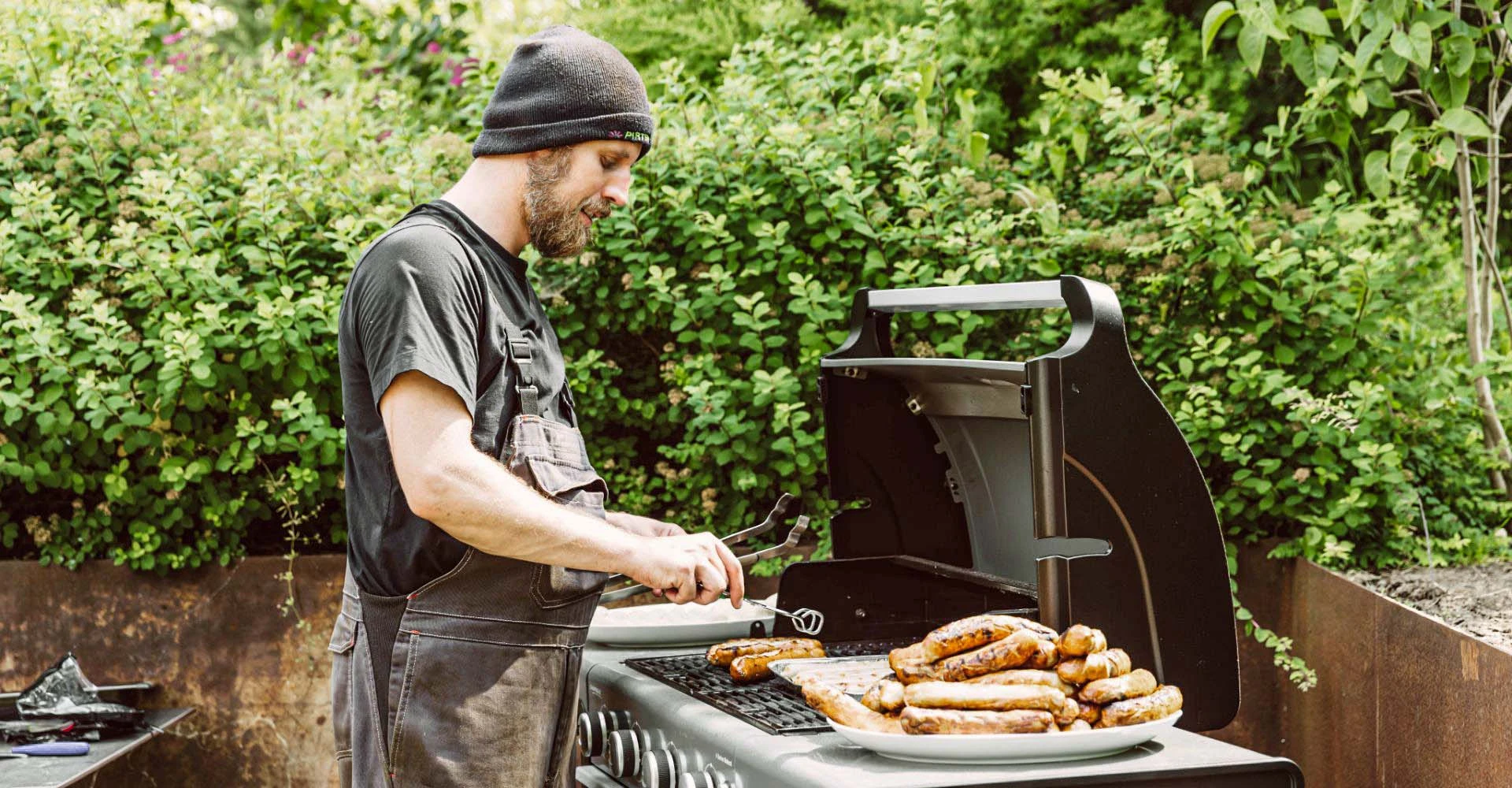 Ein Mitarbeiter von Ehrich steht an einem Grill. Neben ihm ein großer Teller mit Grillwürsten.