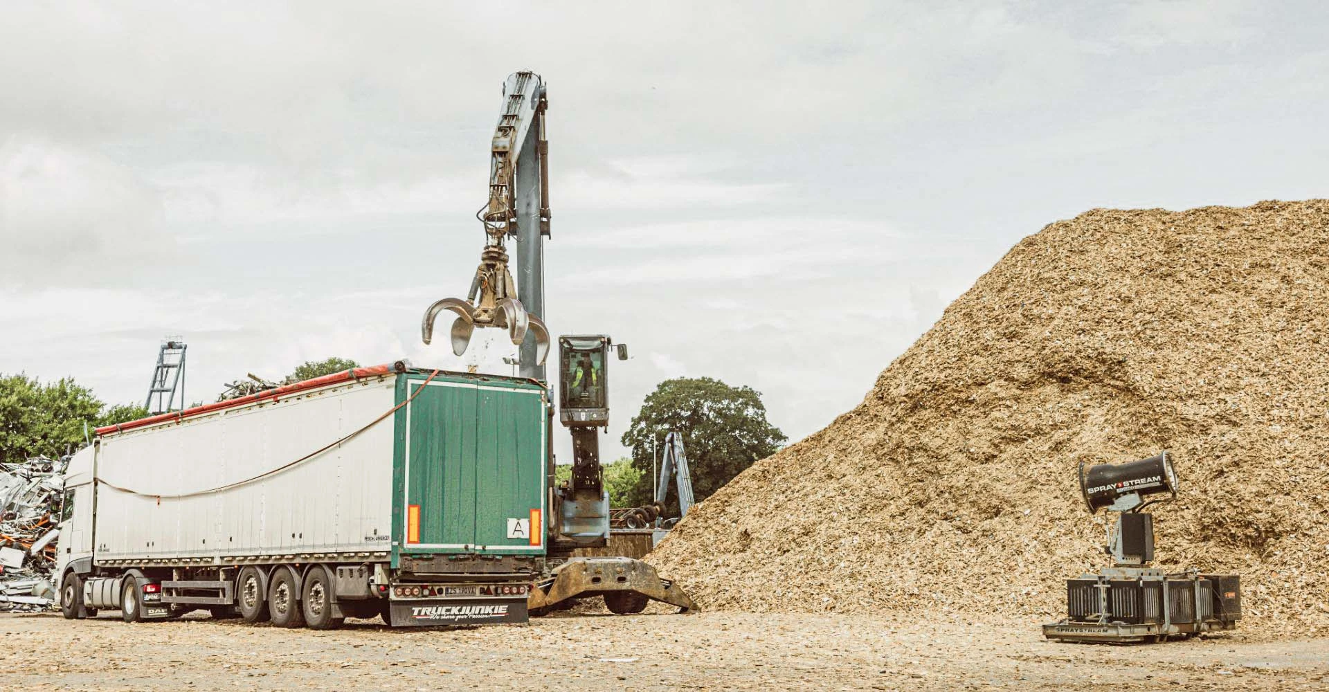 Kranwagen zwischen einem LKW und einem Berg Holzspähne