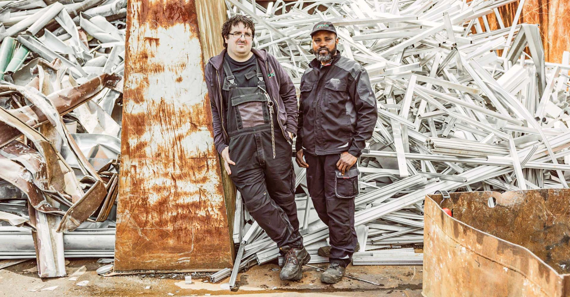 Zwei Mitarbeiter vor einem Haufen Metallschrott