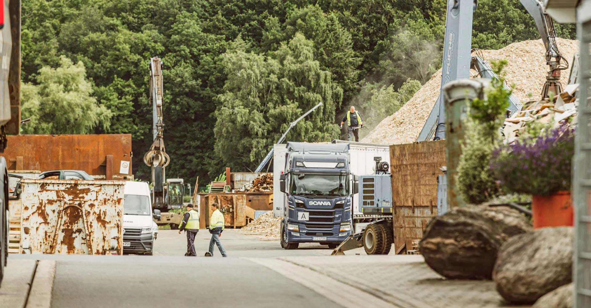 Foto vom Hof mit zwei Mitarbeitern und einem LKW und mehreren anderen Fahrzeugen